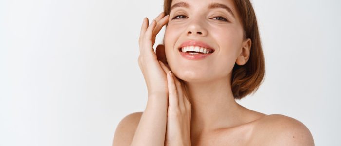 skin-care-beauty-smiling-natural-woman-with-naked-shoulders-healthy-clean-fresh-skin-looking-happy-touching-cheek-girl-apply-facial-cosmetics-white-wall